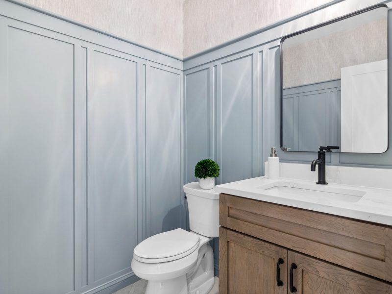 Powder room with wainscoting painted in Benjamin Moore Kentucky Haze AC-16, featuring a wood vanity with a white quartz countertop and a black matte faucet. The design includes a square mirror and minimalist decor for a modern, elegant look.
